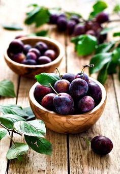 plums in wooden bowls with green leaves on the table