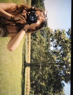 a woman taking a photo with her camera on the grass in front of some trees