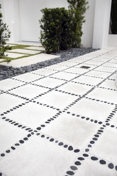 a black and white checkered tile floor in front of a house with bushes on the side