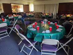 a room filled with tables and chairs covered in green tablecloths, red cups on top of them