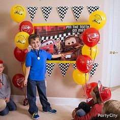 two boys are standing in front of a birthday banner with cars on it and balloons