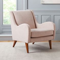 a beige chair sitting on top of a rug in front of a window with blue walls