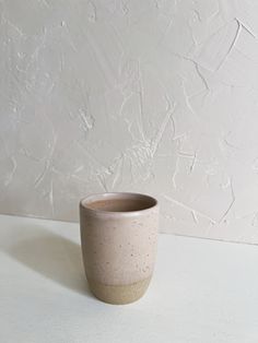 a white and brown cup sitting on top of a table next to a white wall