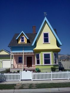 a multi - colored house with white picket fence and blue sky in the back ground