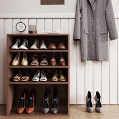 there are many pairs of shoes on the floor next to a coat rack and clock