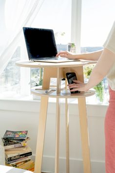 a woman using a laptop computer on top of a wooden table next to a window