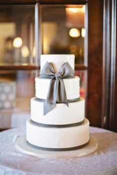 a three tiered white wedding cake with grey ribbon and bow on the top layer