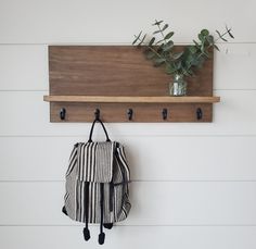 a bag hanging on a wooden shelf next to a potted plant and vase with greenery