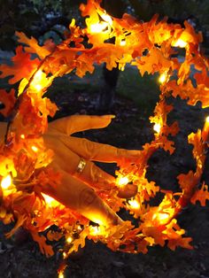 a hand is holding an orange wreath made out of fake leaves and lit with fairy lights