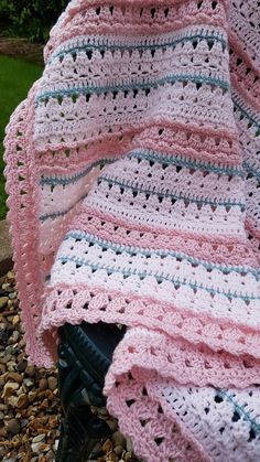 a crocheted blanket sitting on top of a black bench next to some rocks