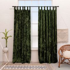 a living room with a chair and window covered in green velvet curtains next to a potted plant