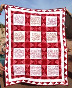 a woman holding up a red and white quilt