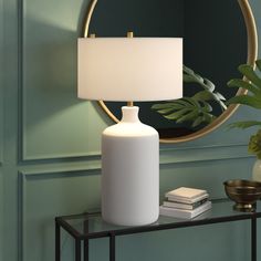 a white lamp sitting on top of a table next to a mirror and potted plant