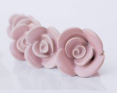 three pink roses sitting next to each other on top of a white surface with one flower in the middle