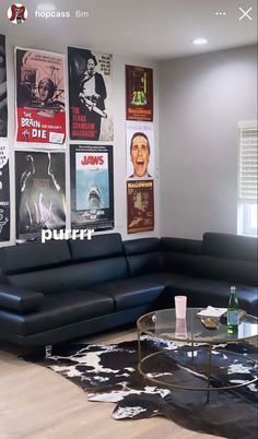 a living room filled with black furniture and posters on the wall above it's glass coffee table