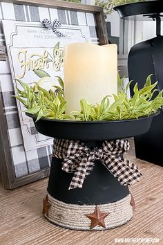 a lit candle sitting on top of a black container filled with greenery and twine