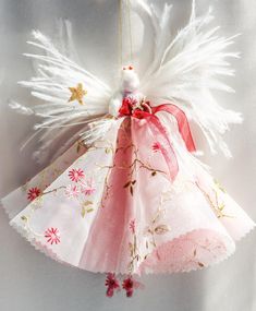 an angel ornament hanging from a string with white feathers and pink flowers on it