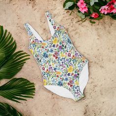 Wrap yourself in the splendor of our Blossom Elegance One-Piece Swimsuit, a perfect blend of style, comfort, and responsible fashion. Adorned with a vibrant, blooming floral pattern, this eco-friendly swimsuit will become your go-to piece for every splashy occasion. Crafted with a stretchy blend of 80% Polyester and 20% Spandex, this suit promises a snug yet comfortable fit that adapts to your movements. The scoop neck and tank straps outline an elegant silhouette, offering modest coverage without sacrificing allure. The built-in bra with soft removable cups provides the support you desire, making it ideal for diverse body types. Whether lounging poolside or riding waves, the UPF 50+ fabric ensures you're shielded from the sun's rays. Handmade with an eye for quality, this one-piece boasts Summer Swimwear With Uv Protection For Sunbathing, Tropical Stretch Swimwear With Upf 50+, Tropical Swimwear For Poolside Warm Weather, Beachy Swimwear With Uv Protection For Sunbathing, Tropical Style Swimwear For Poolside And Warm Weather, Tropical Swimwear For Poolside And Warm Weather, Summer Stretch Swimwear For Warm Weather, Spring Swimwear For Water Sports With Upf 50+, Stretch Swimwear For Vacation