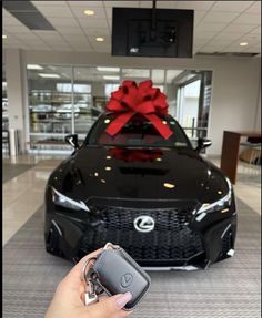 a person holding a car key in front of a black car with a red bow on it