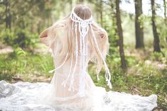 a woman with long blonde hair sitting on a blanket in the middle of a forest