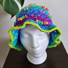 a white mannequin head wearing a crocheted hat with colorful buttons on it