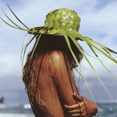 a woman standing on top of a beach next to the ocean wearing a green hat