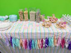 a table topped with lots of candy and desserts next to a green wall in the background