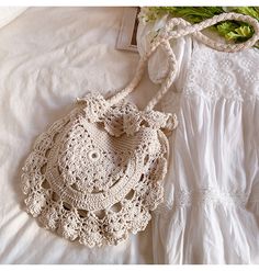 a white crocheted purse sitting on top of a bed next to a bouquet of flowers