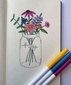 an open notebook with flowers in a mason jar on it and three markers next to it