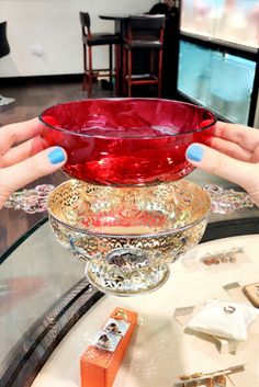 a woman holding a red glass bowl on top of a table