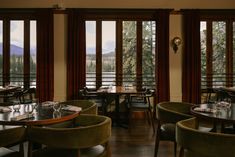 a restaurant with wooden tables and green velvet chairs, overlooking the mountain range outside windows