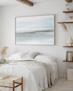 a white bedroom with a large painting hanging on the wall above it's bed