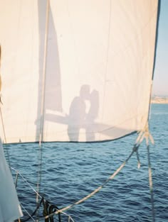 the shadow of two people on a sailboat in the water with their hands behind them