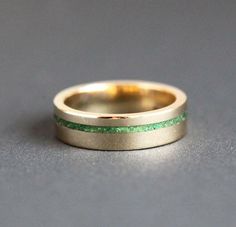 a gold wedding band with green glitter inlays on the outside and inside, sitting on a gray surface