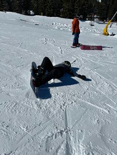 a snowboarder is laying on the ground with his feet in the snow while another person stands behind him