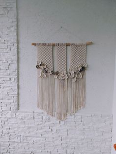 the wall hanging is decorated with flowers and tassels on wooden sticks, along with a white brick wall