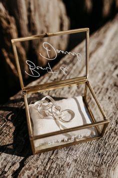 an open box with two wedding rings in it sitting on a piece of drift wood