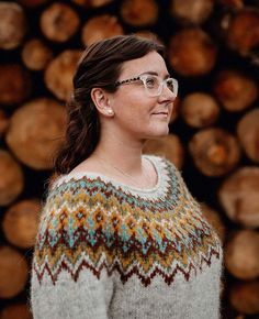 a woman wearing glasses standing in front of logs