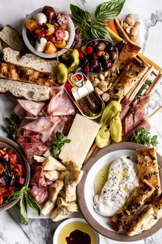 an assortment of meats and cheeses on a platter with olives, tomatoes, bread sticks, crackers, salad dressing, and other condiments