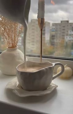 a coffee cup is being poured into a saucer on a window sill in front of a cityscape