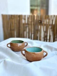 two tea cups sitting on top of a bed