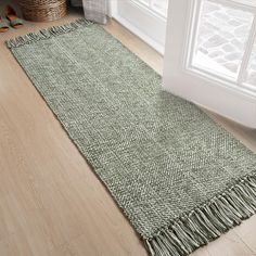 a green rug with fringes on the floor next to a basket and window sill