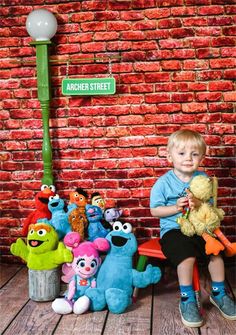 a young boy sitting on a bench with stuffed animals in front of him and a street sign that says ardenen street