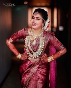 a woman in a red sari with gold jewelry on her neck and hands behind her back