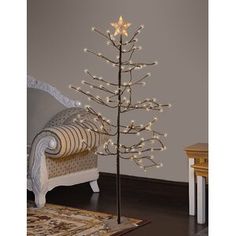 a small christmas tree with lights on it in a living room next to a couch