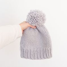 a hand holding a gray knitted beanie with pom - pom on it