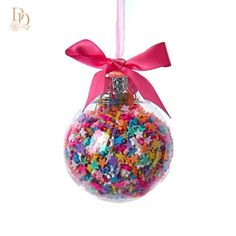 a glass ornament filled with colorful sprinkles and a pink ribbon