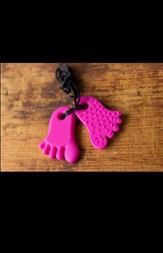 two pink hand and foot shaped key chains on a wooden table with black cord attached