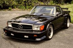 a black mercedes benz sports car parked in a parking lot next to some bushes and trees