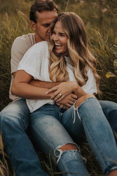 a man and woman sitting on the ground hugging each other in front of tall grass